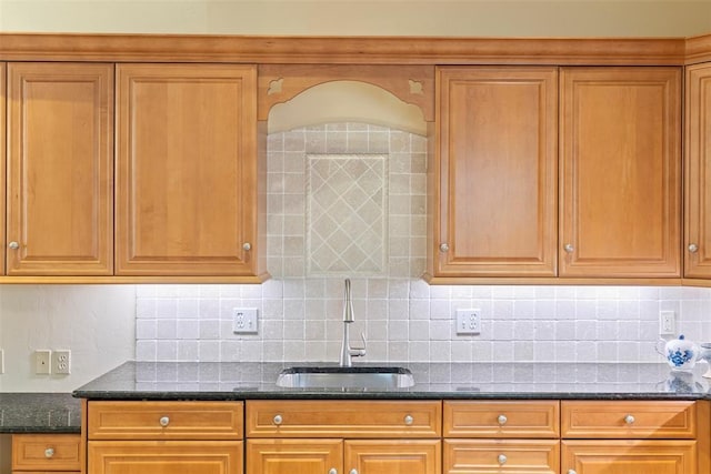 kitchen with decorative backsplash, dark stone counters, and a sink