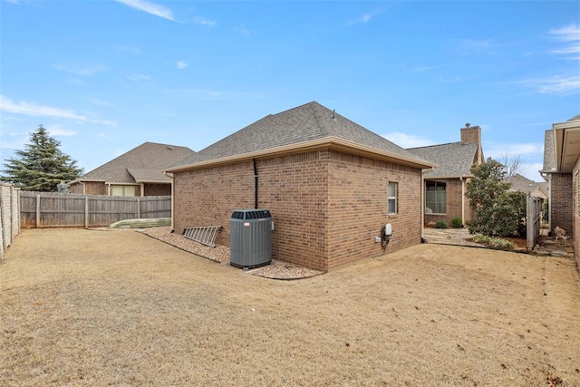 rear view of property with central air condition unit, a fenced backyard, a shingled roof, and brick siding