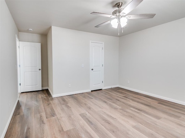 spare room with a ceiling fan, light wood-type flooring, and baseboards