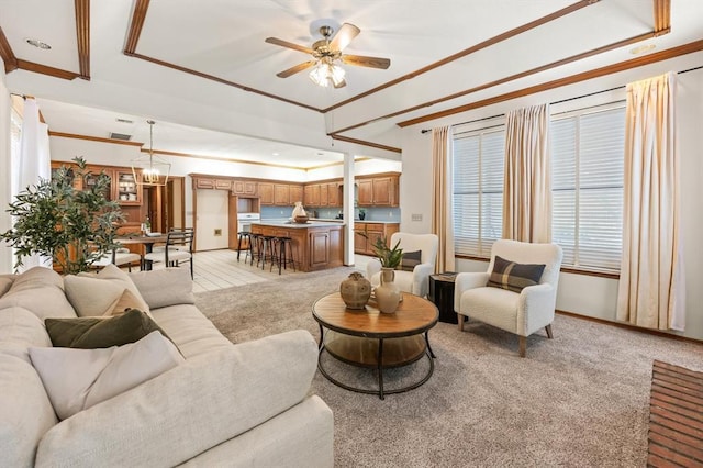 living area featuring light carpet, ornamental molding, a tray ceiling, and ceiling fan with notable chandelier