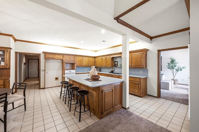 kitchen with light tile patterned floors, light colored carpet, brown cabinets, a center island, and light countertops