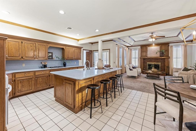 kitchen with a breakfast bar, a center island with sink, light tile patterned floors, light countertops, and open floor plan