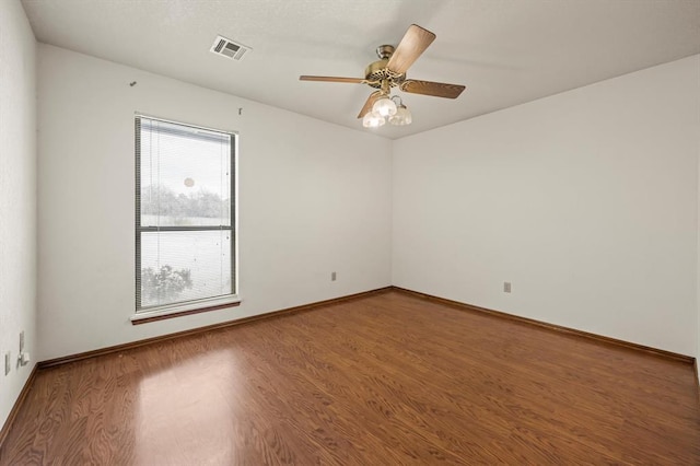 empty room with a ceiling fan, baseboards, visible vents, and wood finished floors