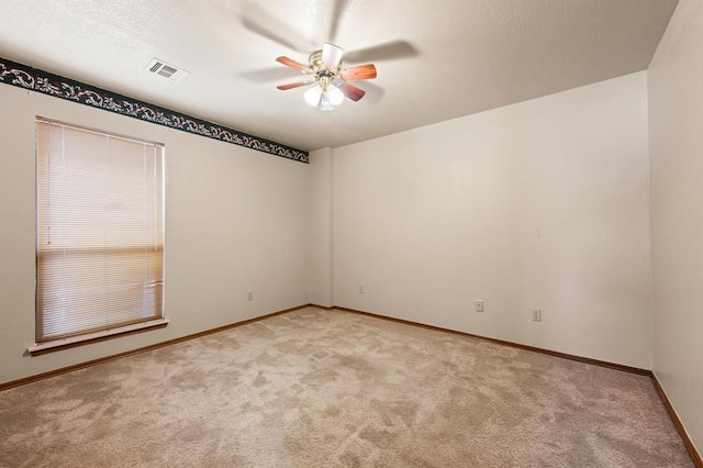 spare room featuring light carpet, ceiling fan, visible vents, and baseboards