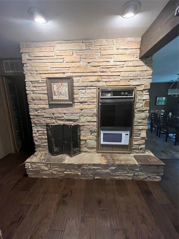 details featuring double oven, a stone fireplace, wood-type flooring, and a textured ceiling