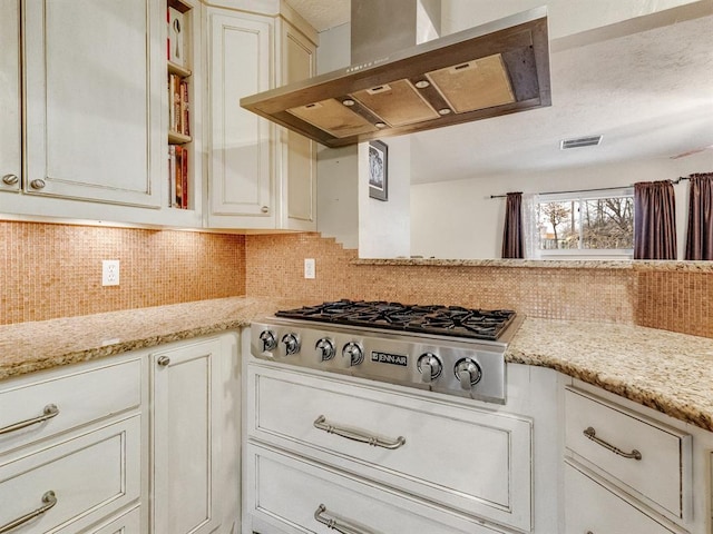 kitchen featuring stainless steel gas stovetop, light stone counters, wall chimney range hood, and backsplash