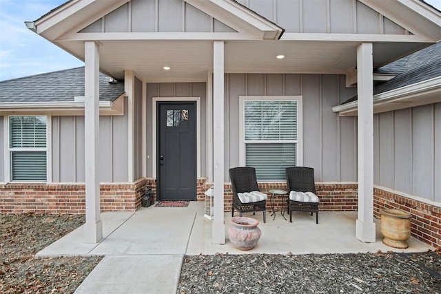 doorway to property with roof with shingles, brick siding, and board and batten siding