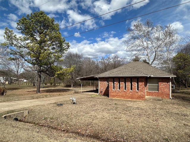 view of home's exterior featuring a carport, brick siding, roof with shingles, and driveway