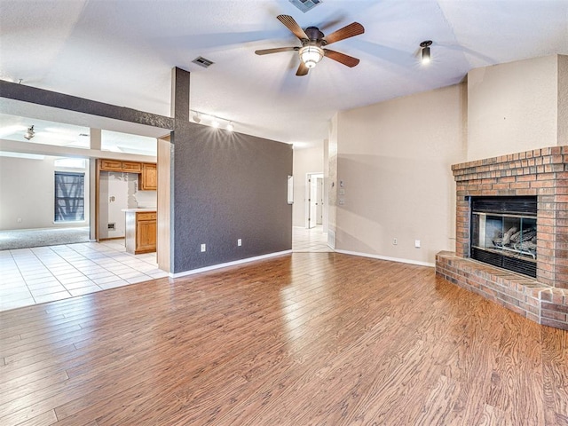 unfurnished living room with a fireplace, ceiling fan, and light wood-type flooring