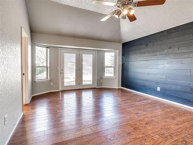 spare room featuring vaulted ceiling, a textured ceiling, ceiling fan, dark wood-type flooring, and wooden walls