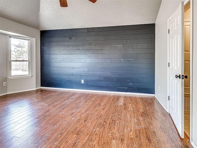 empty room featuring wood walls, ceiling fan, a textured ceiling, and hardwood / wood-style floors