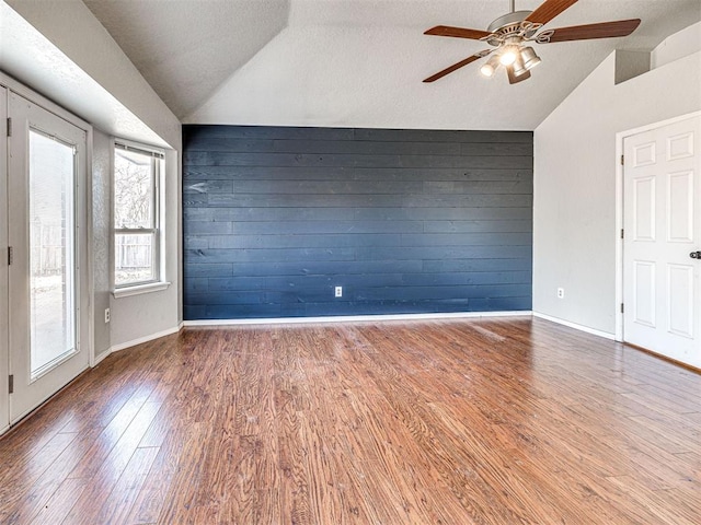 spare room with wood walls, hardwood / wood-style flooring, a textured ceiling, and vaulted ceiling