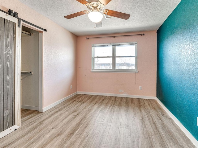 unfurnished bedroom featuring ceiling fan, a barn door, light wood-type flooring, and a textured ceiling