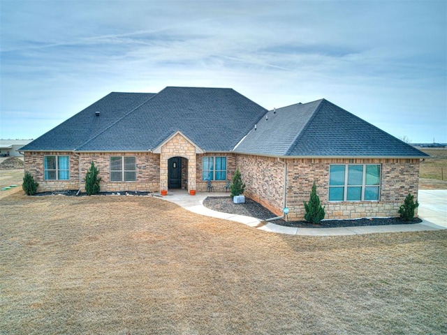 view of front of house with stone siding, a shingled roof, brick siding, and a front yard