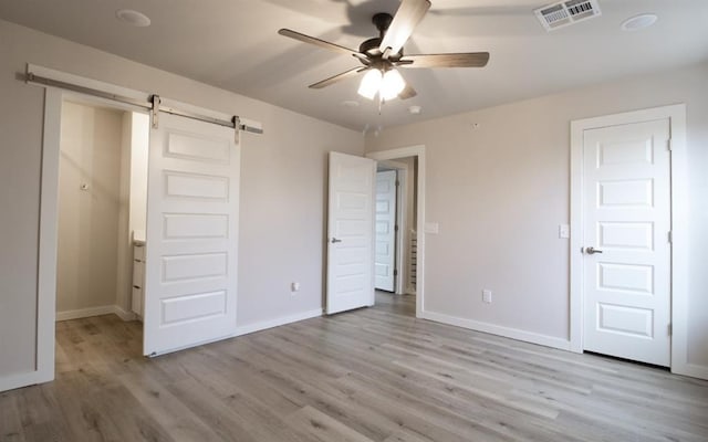 unfurnished bedroom featuring ceiling fan, a barn door, and light hardwood / wood-style flooring