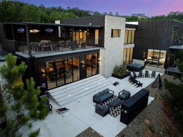 rear view of property with a balcony, stone siding, an outdoor living space, and a patio