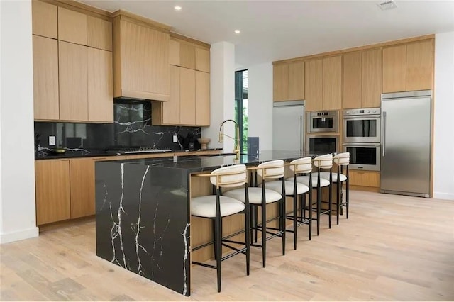 kitchen with dark countertops, light wood-style floors, appliances with stainless steel finishes, and decorative backsplash