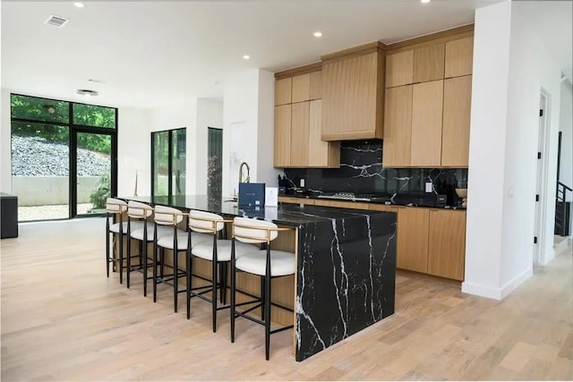 kitchen featuring visible vents, light wood-style floors, backsplash, expansive windows, and a kitchen bar