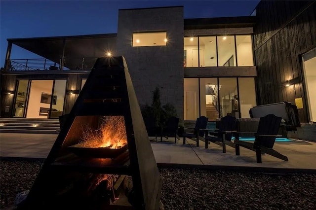 back of house at night featuring a balcony and a patio area