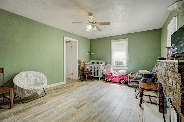 bedroom featuring baseboards, light wood-style flooring, ceiling fan, cooling unit, and a fireplace