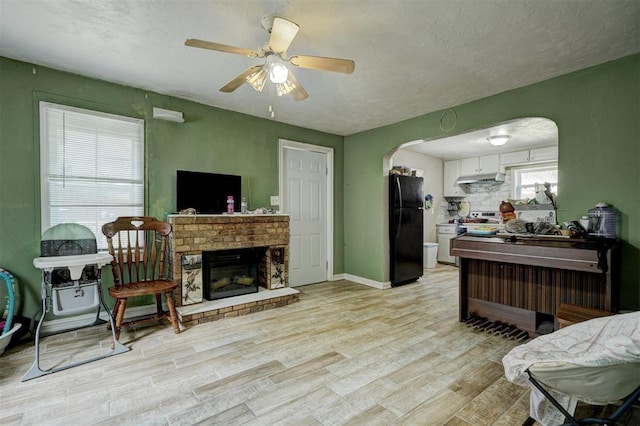 living area with arched walkways, a fireplace, light wood finished floors, ceiling fan, and baseboards