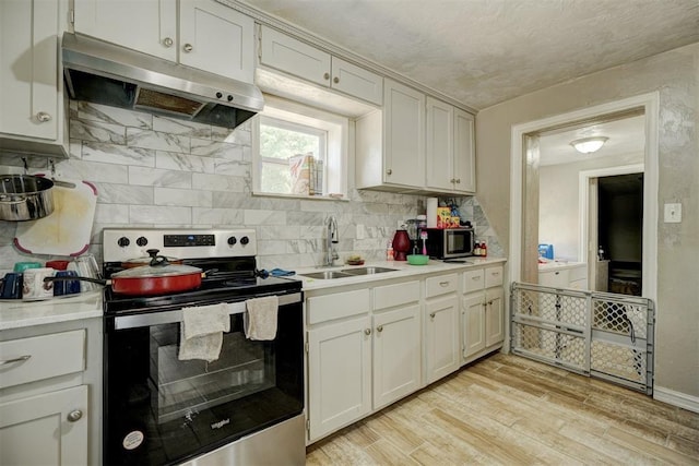 kitchen featuring light countertops, light wood-style flooring, appliances with stainless steel finishes, a sink, and under cabinet range hood