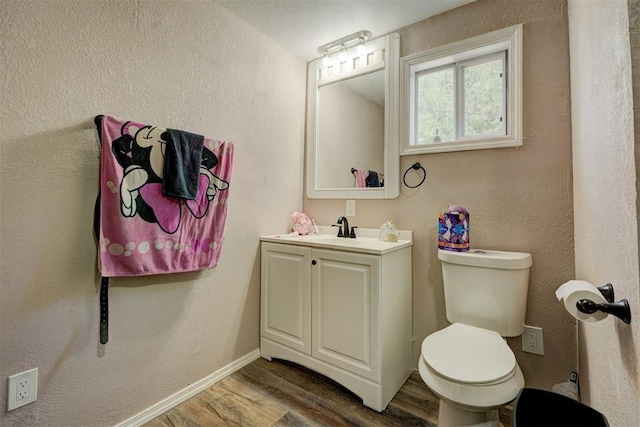 bathroom featuring a textured wall, toilet, wood finished floors, vanity, and baseboards