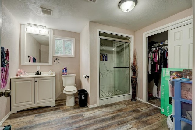 bathroom with a textured ceiling, wood finished floors, a marble finish shower, and vanity