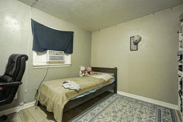 bedroom featuring light wood-style floors, cooling unit, a textured ceiling, and baseboards