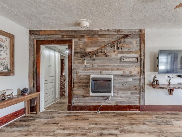 interior space featuring a textured ceiling, wooden walls, heating unit, and wood finished floors