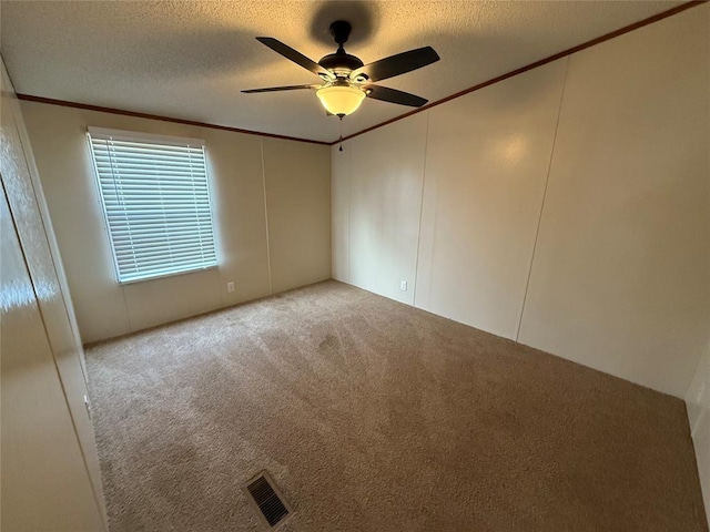 carpeted spare room featuring a textured ceiling, ornamental molding, and ceiling fan