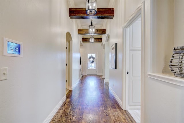 interior space with baseboards, arched walkways, beamed ceiling, and wood finished floors