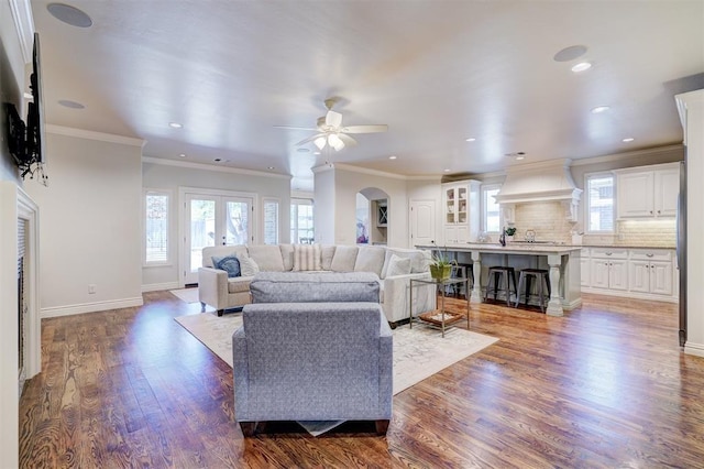 living room featuring arched walkways, ornamental molding, a ceiling fan, wood finished floors, and baseboards