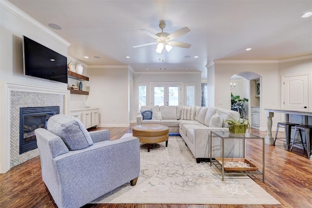 living room featuring arched walkways, ornamental molding, wood finished floors, and a tile fireplace