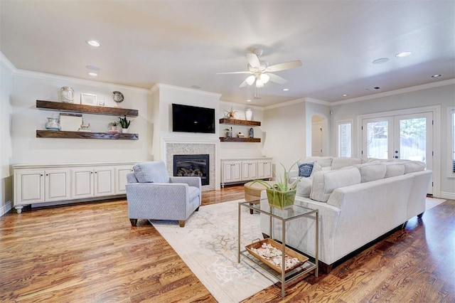 living area with ornamental molding, a glass covered fireplace, french doors, and wood finished floors