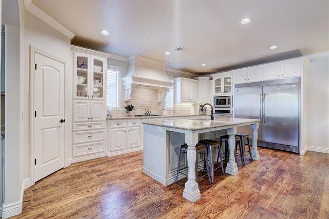 kitchen featuring built in appliances, a sink, light wood-style flooring, and custom range hood