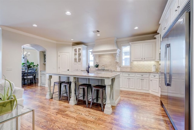 kitchen featuring arched walkways, white cabinets, stainless steel built in fridge, and custom exhaust hood