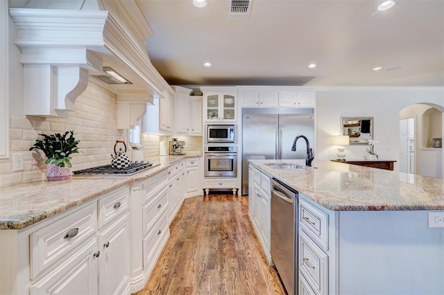 kitchen with arched walkways, visible vents, white cabinetry, a sink, and built in appliances