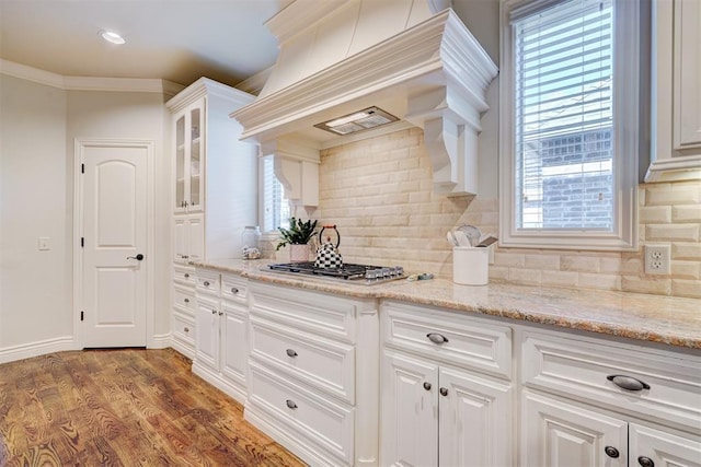 kitchen with premium range hood, wood finished floors, white cabinetry, tasteful backsplash, and glass insert cabinets