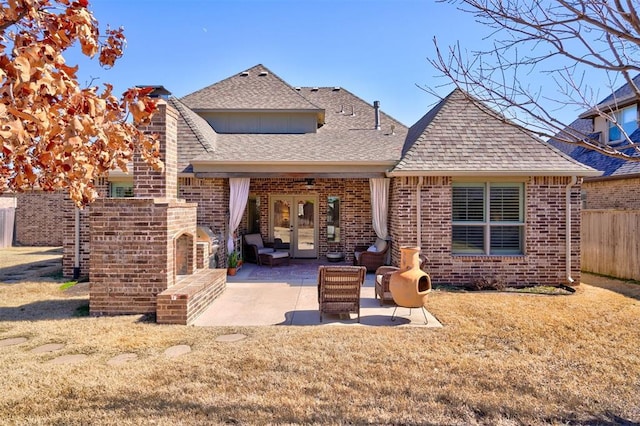 rear view of house with brick siding, a patio, a fireplace, a lawn, and fence