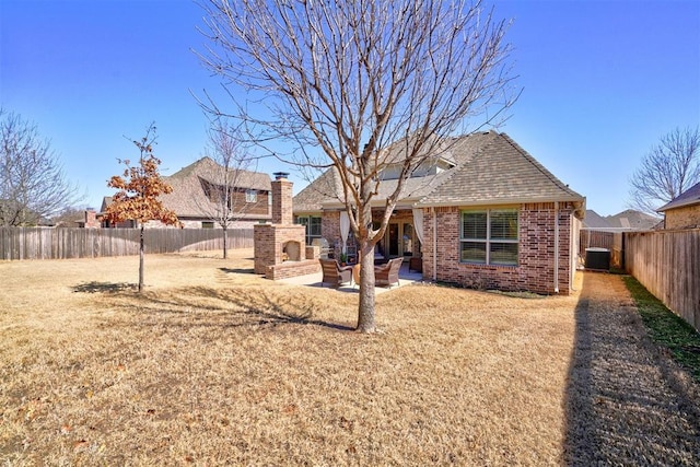 rear view of property featuring a patio area, a fireplace, a fenced backyard, and brick siding