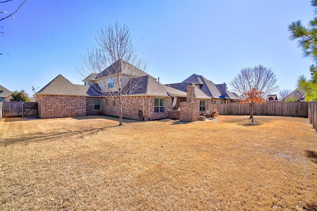 rear view of house featuring a yard, brick siding, and a fenced backyard