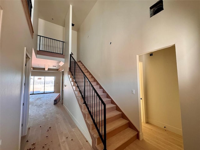 staircase featuring high vaulted ceiling, hardwood / wood-style floors, and baseboards