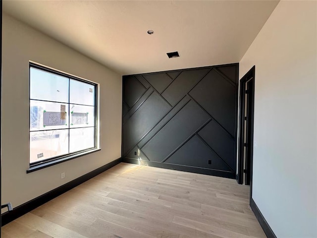 unfurnished room featuring light wood-style flooring, an accent wall, and baseboards