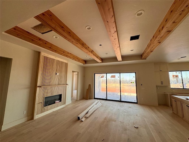 unfurnished living room with light wood-style flooring, baseboards, beam ceiling, and a glass covered fireplace