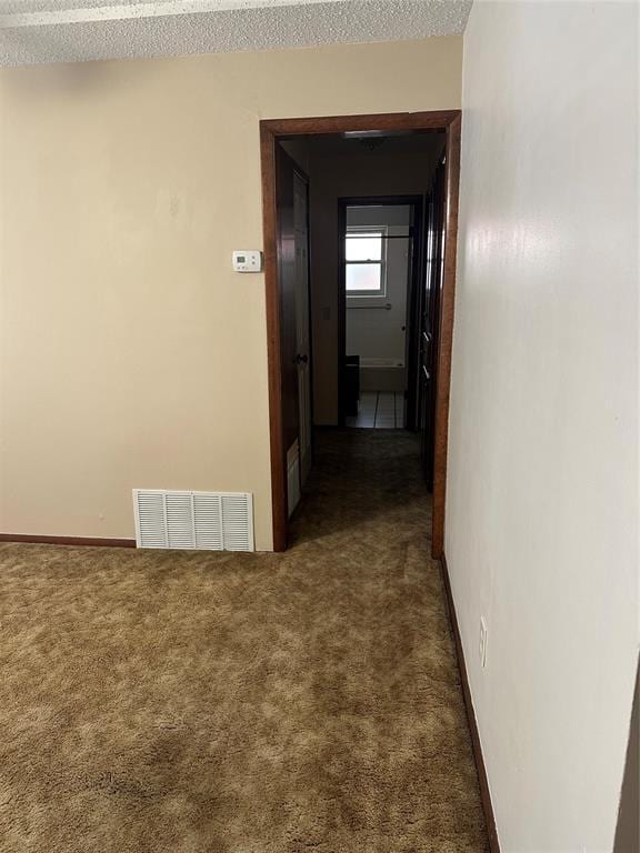 hall with a textured ceiling and dark colored carpet