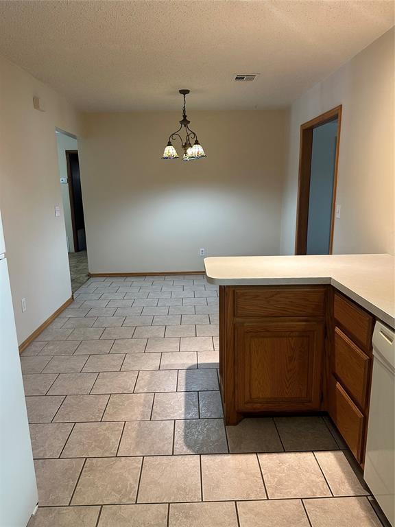 kitchen featuring white dishwasher, light tile patterned floors, a textured ceiling, a chandelier, and pendant lighting