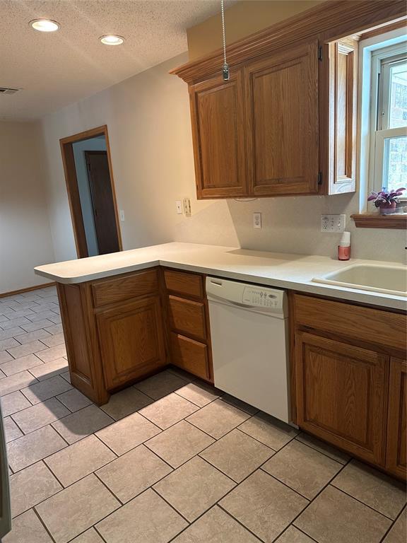 kitchen featuring kitchen peninsula, sink, dishwasher, a textured ceiling, and light tile patterned flooring