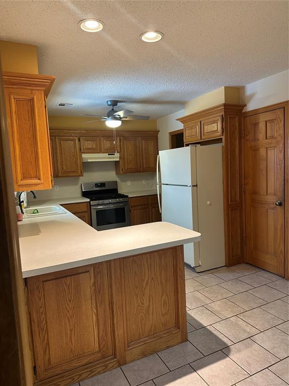 kitchen featuring white fridge, sink, kitchen peninsula, and stainless steel gas range oven