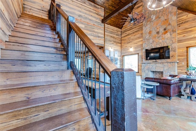 staircase with wood walls, a stone fireplace, ceiling fan, high vaulted ceiling, and wooden ceiling